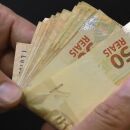 Pessoa com notas de R$ 50,00 na m&atilde;o.