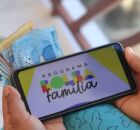 Dinheiro e celular com tela do Bolsa Fam&iacute;lia.