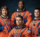 Quatro astronautas est&atilde;o posando juntos, vestindo trajes espaciais laranja. 