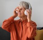Idosa escuta m&uacute;sica com fones em momento de lazer dom&eacute;stico.