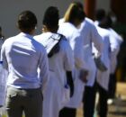 Pessoas com jaleco m&eacute;dico em fila.