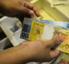 Pessoa contando dinheiro de caixa registradora.