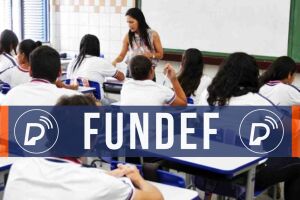 A imagem mostra um professor em sala de aula, com uma tarja com o nome 