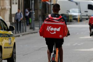 Entregador de aplicativo circula em rua urbana; novo grupo do governo discute garantias para a categoria.