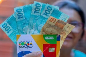 Senhora segurando cart&atilde;o do Bolsa Fam&iacute;lia e dinheiro do benef&iacute;cio.