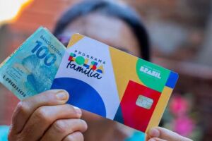 Mulher segurando cart&atilde;o e benef&iacute;cio do Bolsa Fam&iacute;lia.