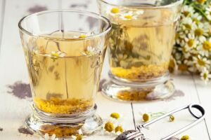 Ch&aacute; de camomila acompanhado de flores frescas, destacando o uso natural da planta para relaxamento e bem-estar.