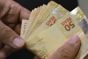Pessoa com notas de R$ 50,00 na m&atilde;o.