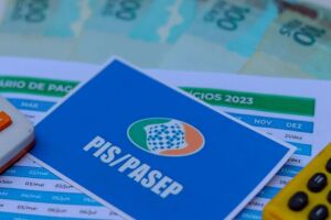 Cart&atilde;o do PIS/Pasep ao lado de dinheiro do abono e calculadoras.