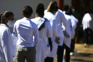 Pessoas com jaleco m&eacute;dico em fila.