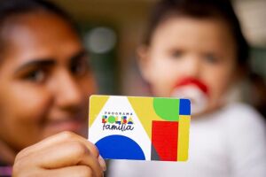 M&atilde;e com beb&ecirc; segurando cart&atilde;o do Bolsa Fam&iacute;lia.