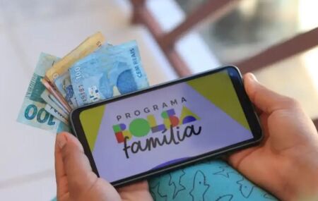 Dinheiro e celular com tela do Bolsa Fam&iacute;lia.