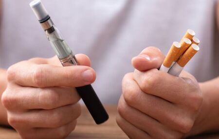 Pessoa segurando ma&ccedil;os de cigarro e vape.