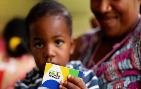 Crian&ccedil;a segurando cart&atilde;o do Bolsa Fam&iacute;lia ao lado da m&atilde;e.