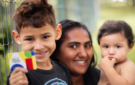 M&atilde;e com seus dois filhos, segurando cart&atilde;o do Bolsa Fam&iacute;lia.
