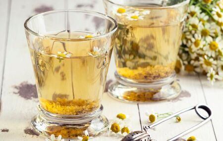 Ch&aacute; de camomila acompanhado de flores frescas, destacando o uso natural da planta para relaxamento e bem-estar.