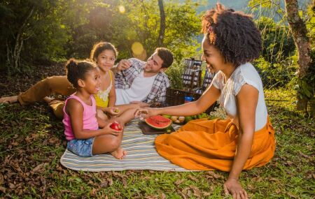 Fam&iacute;lia e crian&ccedil;as em um piquenique no parque durante as f&eacute;rias escolares.