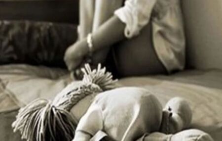 Crian&ccedil;a sentada com boneca ao lado.