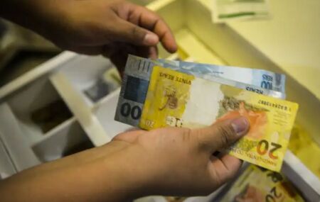 Pessoa contando dinheiro de caixa registradora.