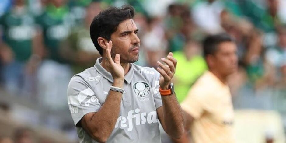 T&eacute;cnico do Palmeiras aplaude &agrave; beira do campo durante partida, uniforme cinza de comiss&atilde;o t&eacute;cnica e torcida ao fundo