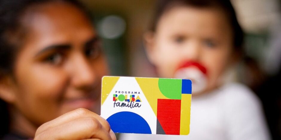 M&atilde;e com beb&ecirc; segurando cart&atilde;o do Bolsa Fam&iacute;lia.